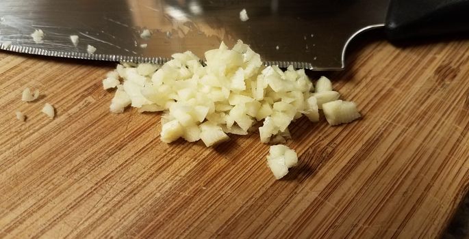 chopped or minced garlic on wood cutting board with knife