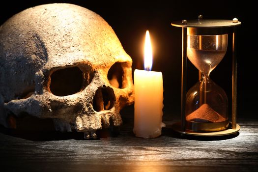 Vintage still life with lighting candle near human skull and hourglass