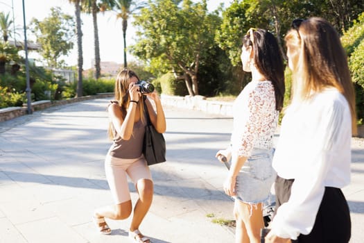 Attractive blonde woman take a picture at her two traveler female friends with a vintage camera in the city - Return to analog technology concept