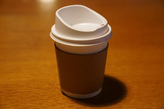 Cup of coffee with paper cup holder on wooden background