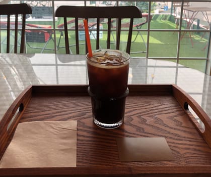 Cup of iced coffee with straw on wooden tray