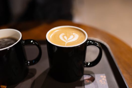 Two cups of coffee with latte art on black tray