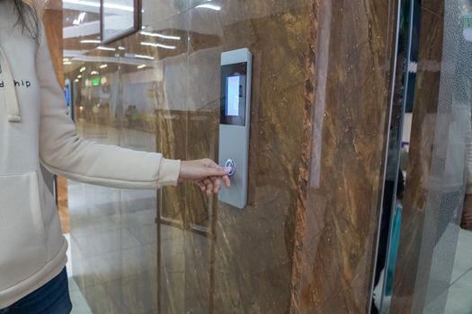 The girl calls the Elevator, ride the Elevator in the office, shopping center or business center to the second floor. The hand presses a button on the tableau with the numbers two