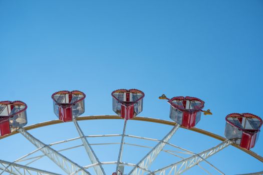 Ferris wheel with cabins in the shape of hearts on a background of blue sky. A romantic walk on the carousel.