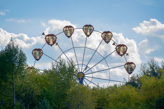 Ferris wheel with cabins in the shape of hearts on a background of blue sky. A romantic walk on the carousel.