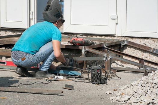 A working welder builds or repairs a new porch and facade of a building or structure. Construction and repair work on the street outdoor. Welder welds metal structure. Construction worker at work