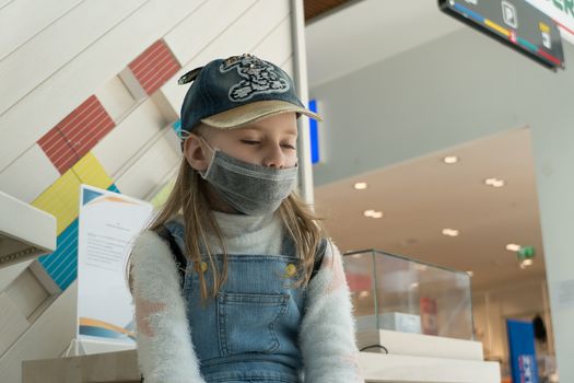 Baby girl with sad eyes in a protective medical mask at the airport during a coronavirus quarantine.
