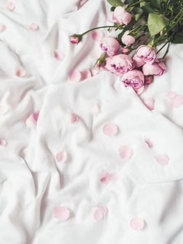 Pink roses and petals on crumpled white fabric. Natural elegant decoration. Romantic background. Top view, flat lay.