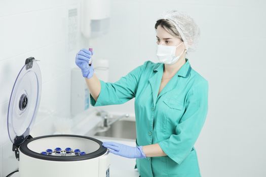 A woman nurse or doctor in a medical mask holds a test tube for a blood test. laboratory centrifuge for the separation of blood components