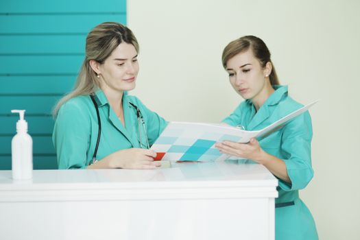 Two female doctor or nurse discussing patient treatment. Stethoscope phonendoscope on the neck. Holds a folder in his hands. Disinfectant on the table