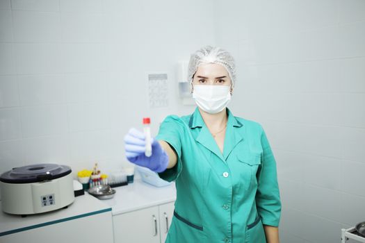 Woman nurse doctor in a medical mask holds a test tube for a blood test