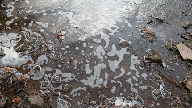 Foamy Water on the side of a river with rocks in the bottom of the frame