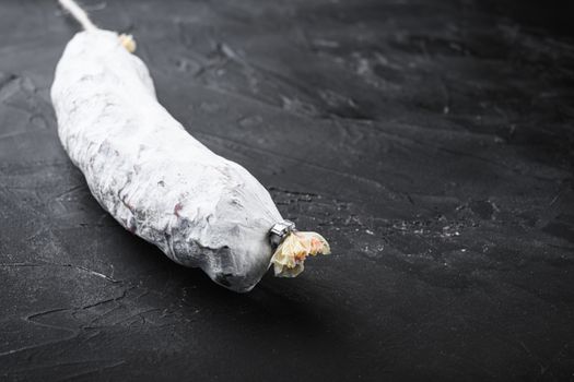 Spanish salchichon dry cured sausage on black surface with copy space.