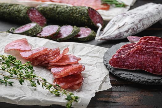 Variety of dry cured chorizo, fuet and other sausages cut in slices with herbs on dark wooden background.