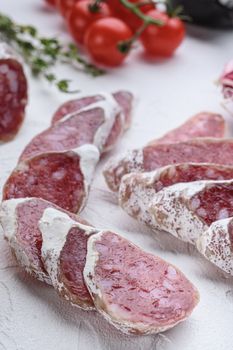 Dry cured fuet salami sausage slices with herbs on white surface.