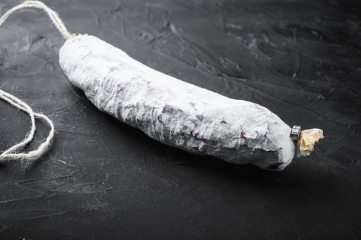 Salchichon, spanish salami sausage on black textured background.