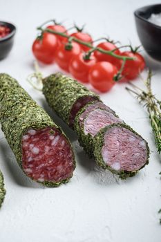 Traditianal fuet sausage in herbs with ingredients on white surface.
