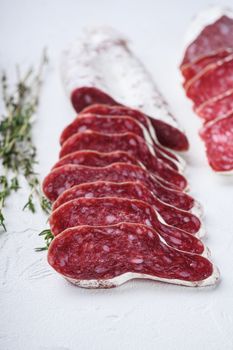 Variety of dry cured fuet and chorizosalami sausages, whole and sliced on white textured background.