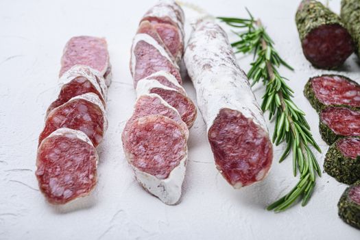 Variety of dry cured fuet and chorizosalami sausages, whole and sliced on white textured background.