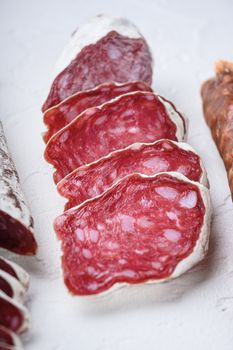 Variety of dry cured fuet and chorizosalami sausages, whole and sliced on white textured background.