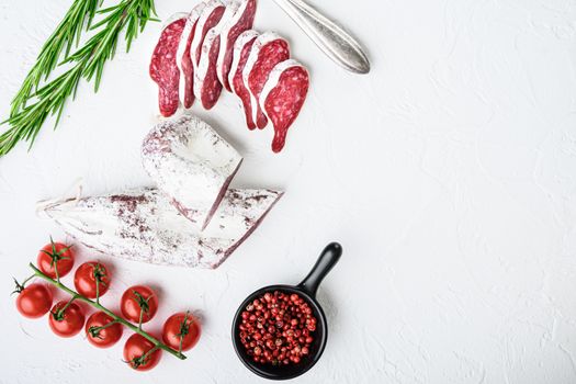 Sliced cuts of longaniza, dry cured spanish sausage with herbs and spices on white surface, top view with copy space.