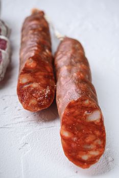 Variety of dry cured fuet and chorizosalami sausages, whole and sliced on white surface.