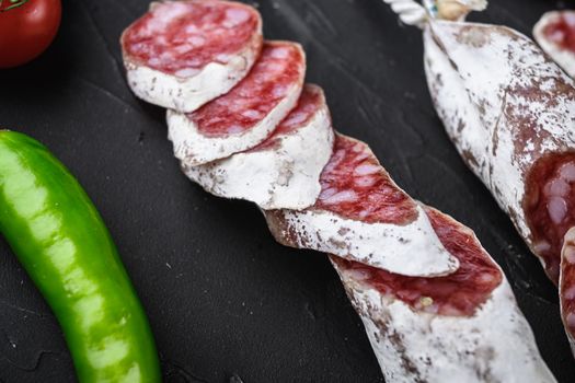 Dry cured fuet salami sausage slices on black textured background.