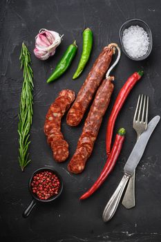 Spanish chorizo sausage slices with herbs and spices on black textured background, topview.