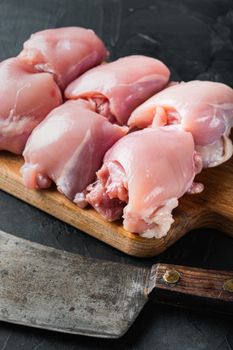 Fresh chicken thighs with meat cleaver, on black background, top view with space for text.
