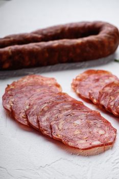 Sliced cuts of chorizo salami sausage on white textured background.
