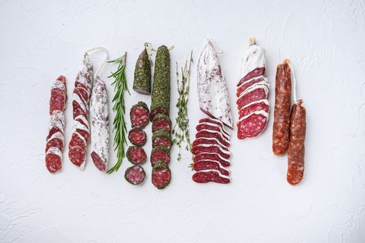 Variety of dry cured fuet and chorizosalami sausages, whole and sliced on white surface, top view.