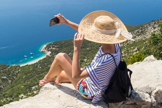 Active sporty woman on summer vacations taking selfie picture while enjoying beautiful coastal view of Cres island, Croatia from Lubenice traditional costal village.