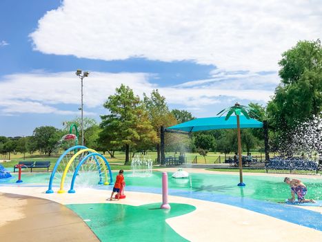 Undefined diverse kids playing at splash park near Dallas, Texas, America in summertime. Colorful recreation site with splashing water fountains for children summertime activities