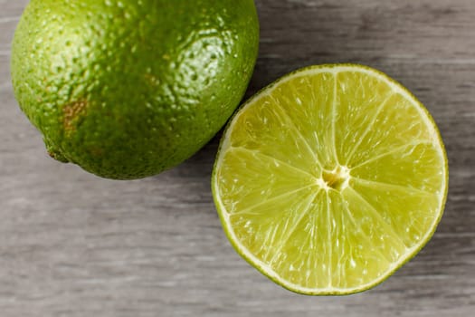 Table top view on green lime cut in half and part of whole one, on a gray wooden table.