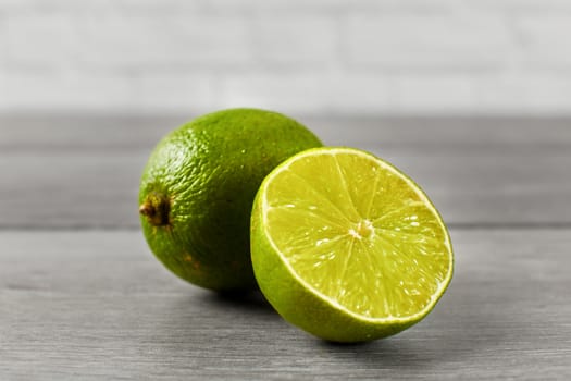 Whole lime and other one cut in half, on a gray wooden table.