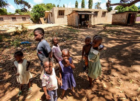 Malindi, Kenya - April 06, 2015:  Group of unknown small kids, standing next to their homes, looking to tourist visiting local slum. Many children suffer under poor living conditions in Kenya.