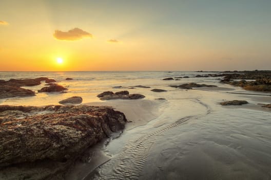 Beach in golden sunset light during low tide showing stream of water and rocks covered with sea algae. Kantiang Bay, Ko Lanta, Thailand.