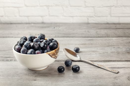 Small bowl of black blueberries with spoon next to it, placed on a gray wood table