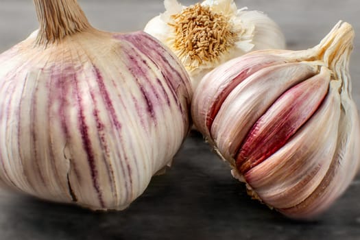 Detailed photo of garlic bulbs on wooden table, some purple cloves uncovered under garlic skin.