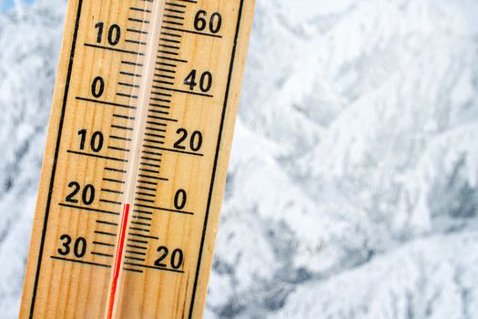 Detail of thermometer showing freezing 20 degrees Celsius sub zero, with blurred snow covered trees in background. Concept illustrating extreme cold weather.