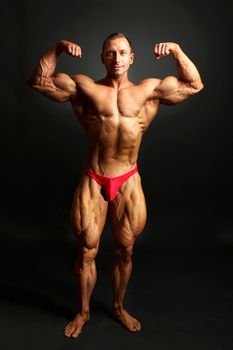Male bodybuilder posing, showing front body muscles, studio shot on black background.