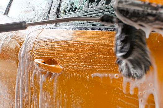 Detail of dark yellow car side washed in carwash. Brush leaving strokes in white soap and shampoo foam.