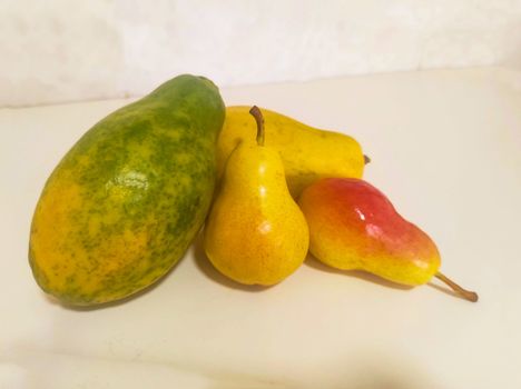 Close up of papaya and pear on light background. Whole ripe yellow fruits.