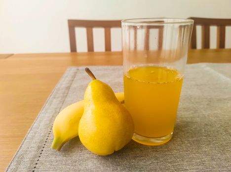 Banana, pear and glass of orange juice, on fabric towel, on the table and blurred background.