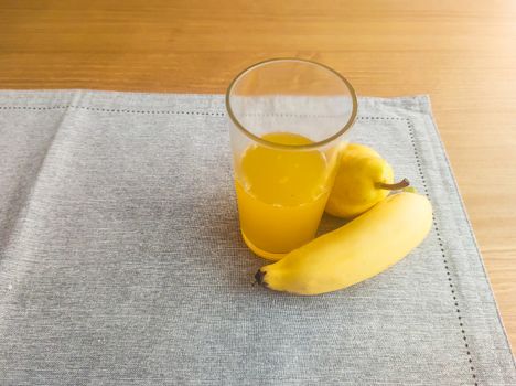 Banana, pear and glass of orange juice, on fabric towel, on the table and blurred background.
