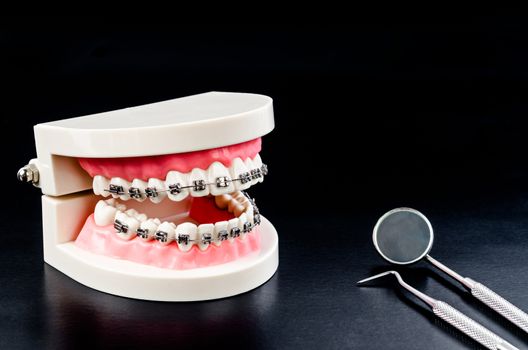 Set of metal Dentist's medical equipment tools with model teeth on black background.