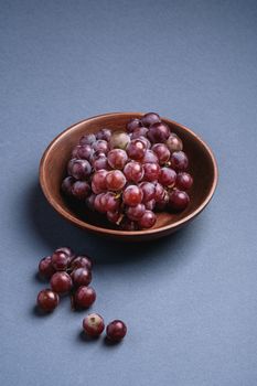 Fresh ripe grape berries in brown wooden bowl on blue grey minimal background, angle view