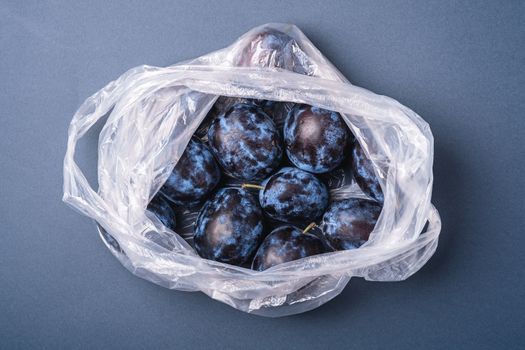 Fresh ripe plum fruits in plastic bag package on blue grey minimal background, top view