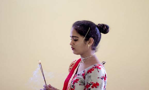 A beautiful young Hindu girl with Incense sticks burning with smoke and gold ornaments according to her traditions and customs , blur background