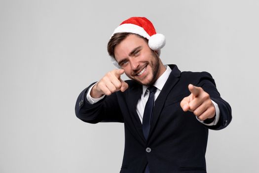 Young handsome caucasian guy in business suit and Santa hats on white background in studio smilie and showing Finger to the camera. Close up portrait business person with Christmas mood Holiday banner